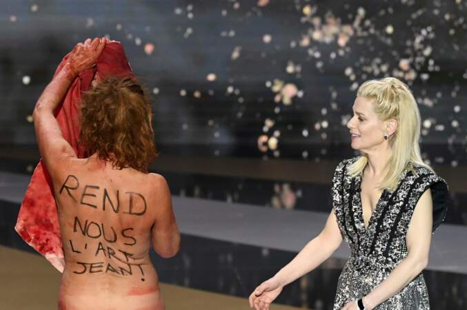 Quelques secondes plus tard, elle est cette fois totalement nue avec, sur sa poitrine, le slogan "No culture, no future", et sur son dos, l’inscription "Rend-nous l’art, Jean". 